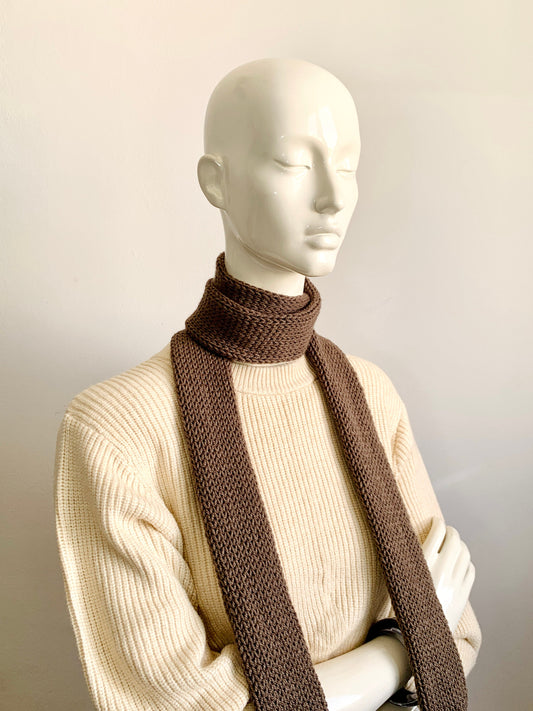 A mannequin displaying a light brown skinny knit scarf in a double tube style, worn with a pale brown long-sleeve top.