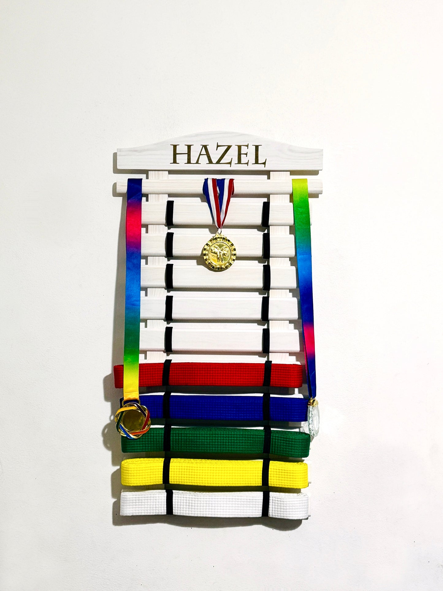 personalized wooden karate belt display rack in white color with engraved name holding colored belts and medals