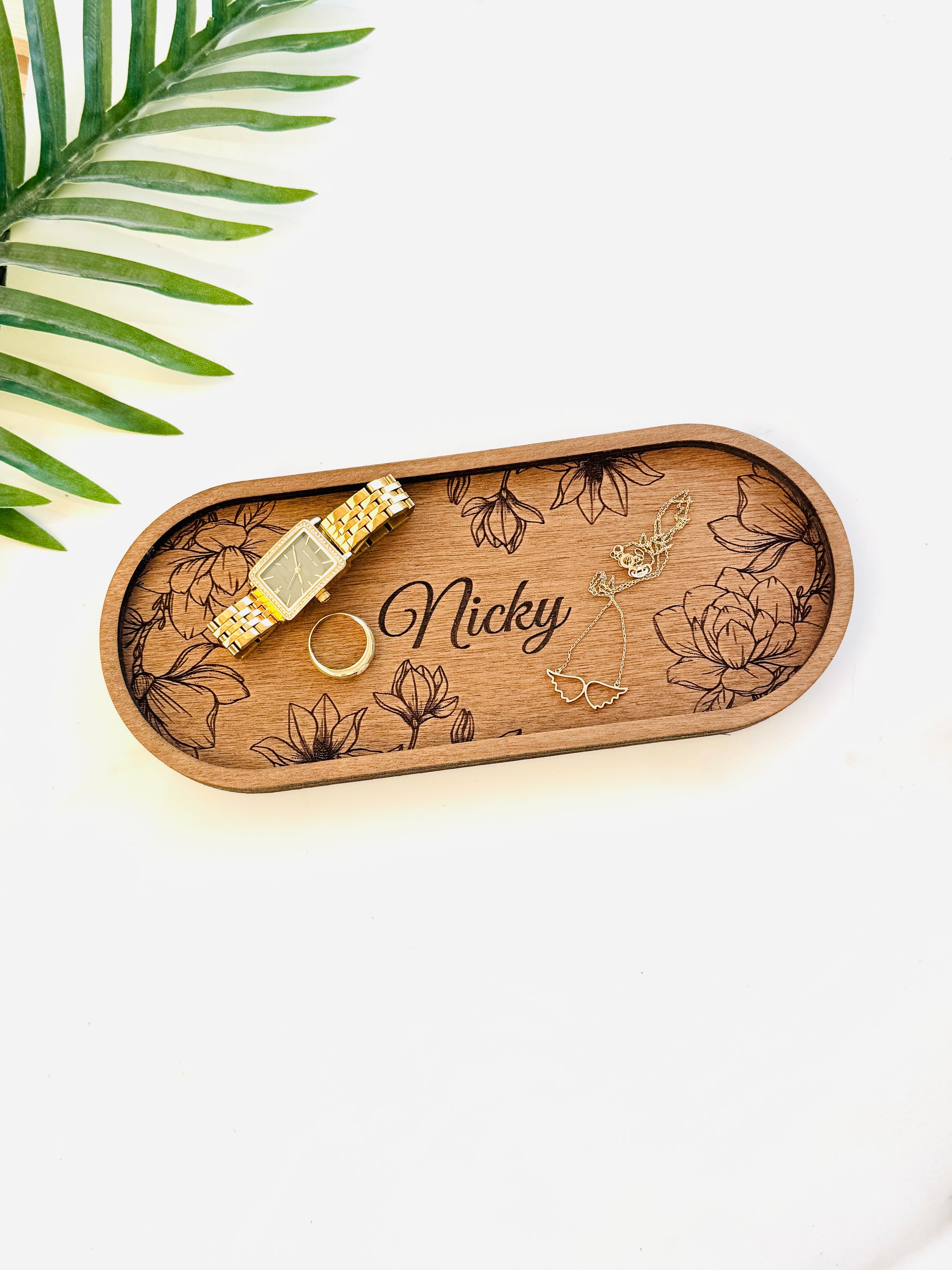 Wooden tray with floral designs and engraved name, featuring a gold watch and ring on a white background.